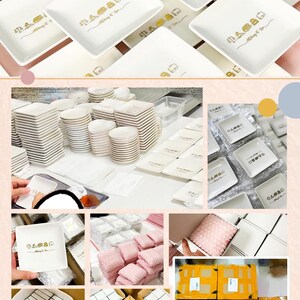 May include: A collection of white square ceramic dishes featuring a gold graphic print of a house icon and the text "Always & Co". The set includes stacks of dishes, individual pieces, and items packaged in boxes with pink protective foam.