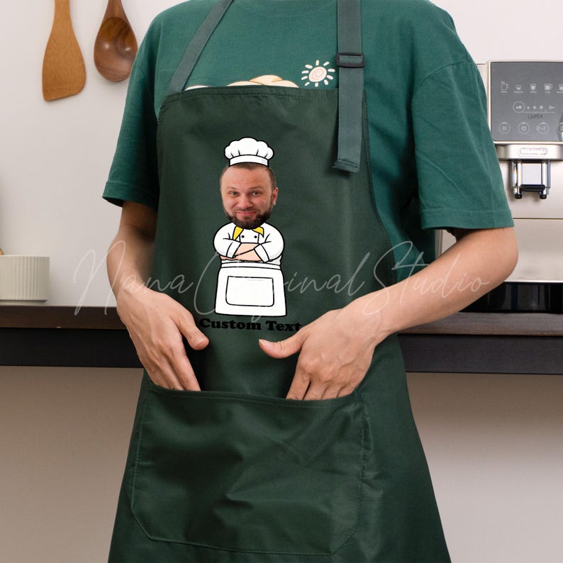 May include: Dark green apron with a cartoon chef graphic. The chef graphic has a person's face, a white chef's hat, and a yellow bow tie. The apron has a large front pocket and adjustable neck strap. The text "Custom Text" is below the chef graphic.