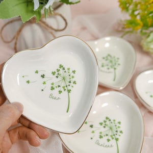Puede incluir: Conjunto de cuatro platos de cerámica blanca en forma de corazón con ribete dorado. Cada plato presenta un diseño de diente de león verde con las palabras "Bear" y "Dandelion" escritas en ellos.