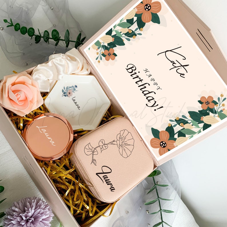 Puede incluir: Una caja de regalo rosa llena de art&iacute;culos personalizados, que incluyen un peque&ntilde;o espejo, un porta anillos y una peque&ntilde;a bolsa. La caja est&aacute; decorada con un patr&oacute;n floral y el texto "&iexcl;Feliz cumplea&ntilde;os! Katie".