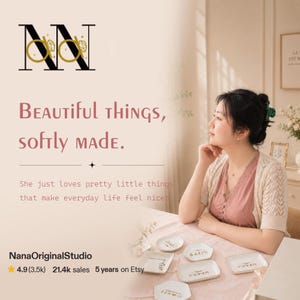K&ouml;nnte beinhalten: Das Bild zeigt eine Frau, die an einem Tisch sitzt, auf dem sich mehrere kleine, wei&szlig;e Keramikschalen befinden. Die Schalen haben goldfarbene Schrift. Der Text auf dem Bild lautet "Beautiful things, softly made." und "NanaOriginalStudio".