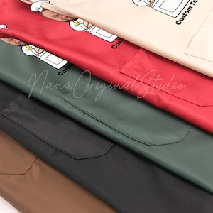 May include: A close-up of several aprons in various colors: tan, red, green, black, and brown. Each apron has a pocket and a custom graphic of a chef. The text "Custom Text" is printed on the tan apron.
