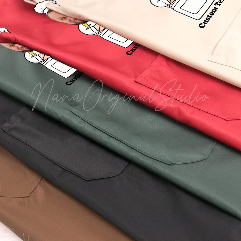 May include: A close-up of several aprons in various colors: tan, red, green, black, and brown. Each apron has a pocket and a custom graphic of a chef. The text "Custom Text" is printed on the tan apron.