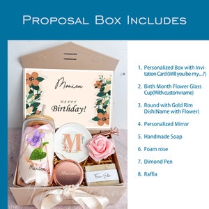 May include: A gift box with a personalized invitation card, glass cup, dish, mirror, soap, foam rose, pen, and raffia. The box includes a card that says "Happy Birthday!" and the name "Monica". The box is beige and has a ribbon.