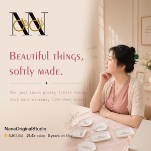 May include: The image features a woman seated at a table with several small, white ceramic dishes. The dishes have gold lettering. Text on the image reads "Beautiful things, softly made." and "NanaOriginalStudio".