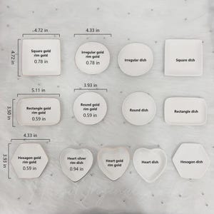 May include: A collection of white ceramic dishes in various shapes: square, irregular, round, rectangle, hexagon, and heart. Some dishes have gold rims. Measurements are in inches, with the largest square dish at 4.72 inches.