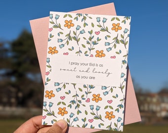 May include: A white card with a floral pattern and the text "I pray your Eid is as sweet and lovely as you are". The card is folded in half and has a pink envelope.