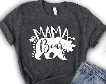 May include: A dark gray t-shirt with the text "Mama Bear" in white lettering. The text is accompanied by a white silhouette of a bear with an arrow pointing to the right.