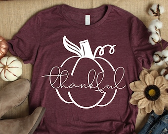 May include: A maroon t-shirt with a white pumpkin graphic and the word "thankful" written in a cursive font.