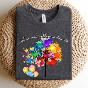 May include: A dark grey t-shirt with a colorful tree design and the text "Love with all your heart". The tree is made up of colorful paint splatters and has butterflies flying around it.