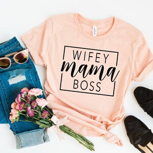 May include: A peach-colored t-shirt with the text "WIFEY mama BOSS" printed in black inside a black square.