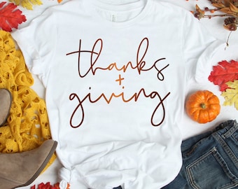 May include: White t-shirt with the words "thanks + giving" in a brown script. The shirt is styled with blue jeans, brown boots, a yellow knit sweater, and fall foliage including orange and red leaves and a small pumpkin.