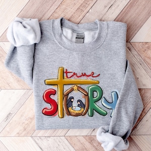 May include: A gray sweatshirt with a colorful graphic design that says "true story" with a depiction of the nativity scene.