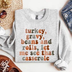 May include: Gray sweatshirt with the text "turkey, gravy, beans and rolls, let me see that casserole" in colorful retro font.