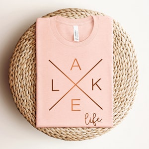 May include: A pink t-shirt with a copper-colored graphic that says "lake life" with the letters "lake" in a cross design.