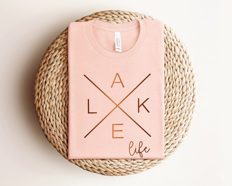 May include: A pink t-shirt with a copper-colored graphic that says "lake life" with the letters "lake" in a cross design.