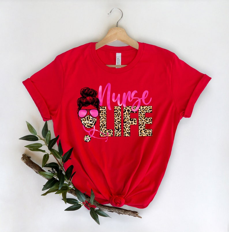May include: Red t-shirt with a pink and black leopard print design that says "Nurse Life". The design features a woman with a bun in her hair wearing a face mask and sunglasses.