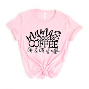 Puede incluir: Camiseta rosa con texto negro que dice "mama needs coffee lots & lots of coffee" y una ilustraci&oacute;n en blanco y negro de una taza de caf&eacute;.