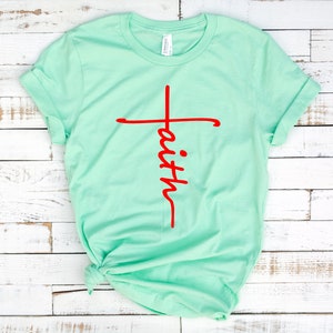 May include: A light green t-shirt with a red cross and the word "faith" written vertically down the cross.