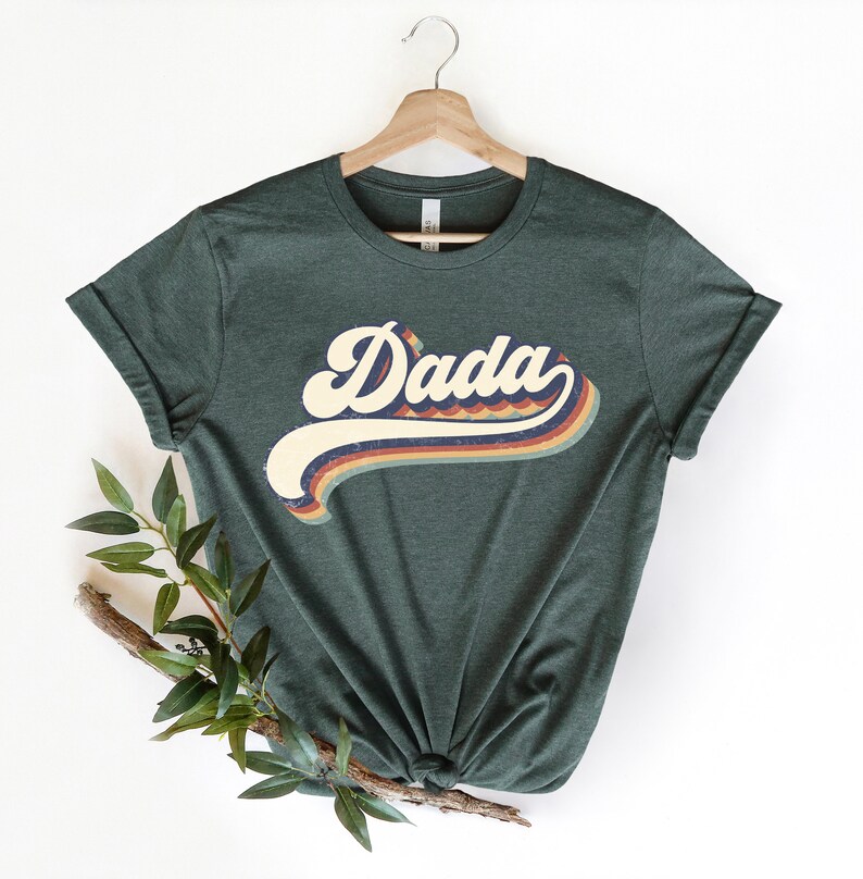 Może przedstawiać: Zielony T-shirt z grafiką w stylu retro, na kt&oacute;rej widnieje napis "Dada" w kolorowym, falistym foncie.