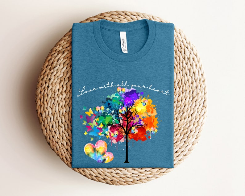 May include: A teal blue t-shirt with a colorful watercolor tree and butterflies. The text "Love with all your heart" is written in white script on the shirt.