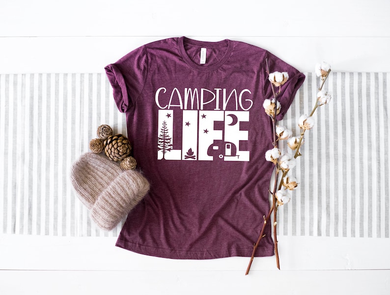 May include: A maroon t-shirt with the text "Camping Life" in white. The text is surrounded by images of a campfire, a camper, a moon, and stars.
