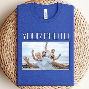 Puede incluir: Una camiseta azul real con el texto "YOUR PHOTO" encima de una imagen rectangular de un grupo de personas. La imagen muestra a un grupo de personas sonriendo y saludando a la cámara. La camiseta está sobre una superficie tejida.