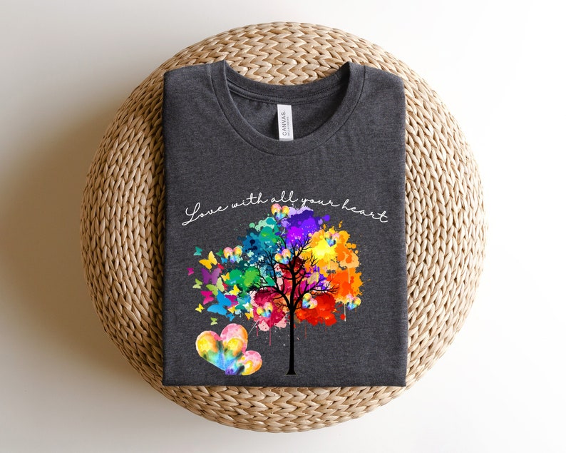 May include: A dark grey t-shirt with a colorful tree design and the text "Love with all your heart". The tree is made up of colorful paint splatters and has butterflies flying around it.