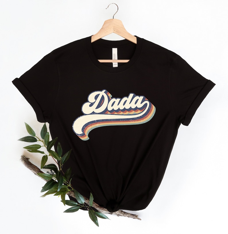 Może przedstawiać: Czarny T-shirt z grafiką w stylu retro, na kt&oacute;rej widnieje napis "Dada" w kolorach tęczy.