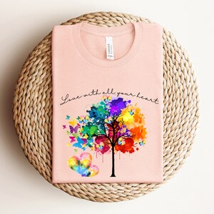 May include: A pink t-shirt with a watercolor tree design and butterflies. The text "Love with all your heart" is printed on the shirt.