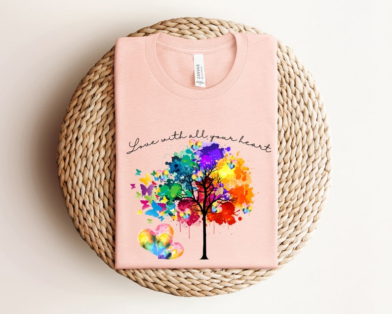 May include: A pink t-shirt with a watercolor tree design and butterflies. The text "Love with all your heart" is printed on the shirt.