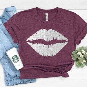 May include: A maroon t-shirt with a white glitter-like lip print design.
