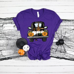 May include: Purple t-shirt with a graphic of three gnomes riding in the back of a black pickup truck with pumpkins. The gnomes are wearing Halloween costumes.