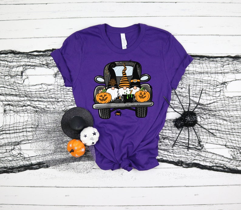 May include: Purple t-shirt with a graphic of three gnomes riding in the back of a black pickup truck with pumpkins. The gnomes are wearing Halloween costumes.