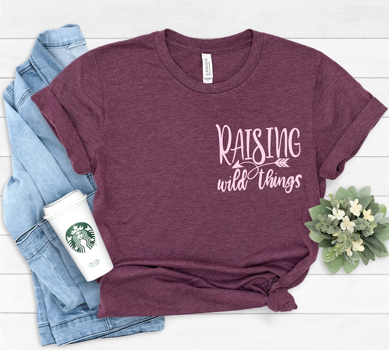 May include: A maroon t-shirt with the text "Raising wild things" in pink lettering with an arrow pointing to the right.