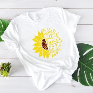 May include: White t-shirt with a yellow sunflower graphic and the text "In a world full of roses be a sunflower".