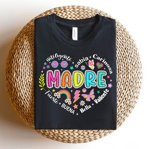 Puede incluir: Camiseta negra con un dise&ntilde;o gr&aacute;fico colorido que dice "MADRE" rodeado de palabras como "inteligente", "sabia", "cari&ntilde;osa", "fuerte", "buena", "bella" y "valiente".