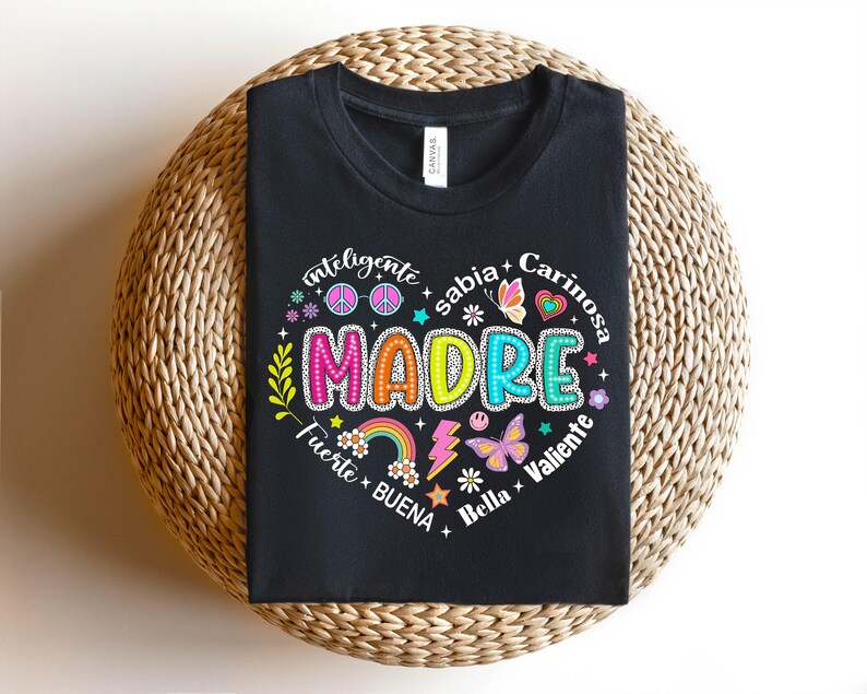 Puede incluir: Camiseta negra con un dise&ntilde;o gr&aacute;fico colorido que dice "MADRE" rodeado de palabras como "inteligente", "sabia", "cari&ntilde;osa", "fuerte", "buena", "bella" y "valiente".