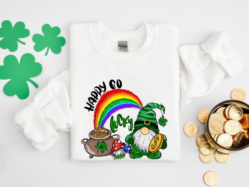 May include: A white sweatshirt with a green leprechaun holding a pot of gold and a rainbow with the words 'Happy Go Lucky' printed on it