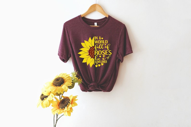 May include: A maroon t-shirt with a yellow sunflower graphic and the text "In a world full of roses be a sunflower".
