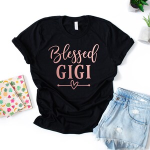 May include: Black t-shirt with the text "Blessed Gigi" in rose gold lettering and a small heart design.