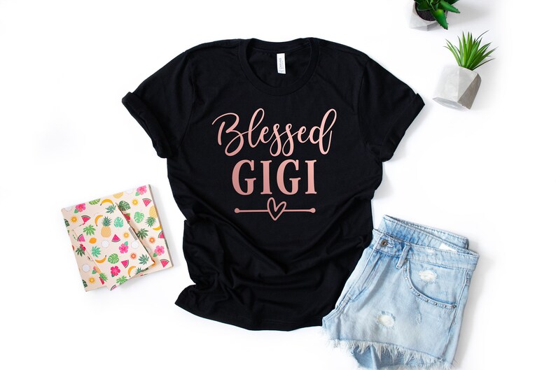 May include: Black t-shirt with the text "Blessed Gigi" in rose gold lettering and a small heart design.