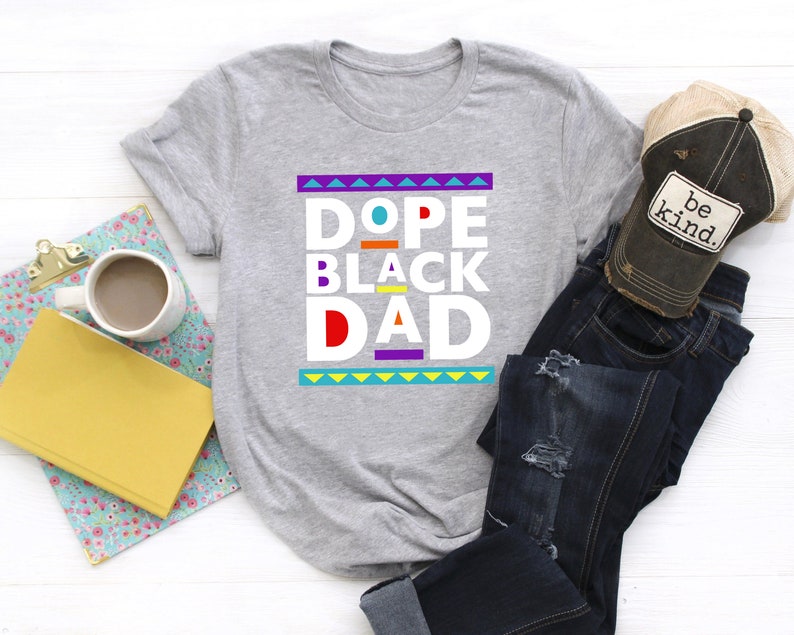 May include: Gray t-shirt with the text "Dope Black Dad" in colorful block letters. The text is surrounded by a colorful geometric pattern.