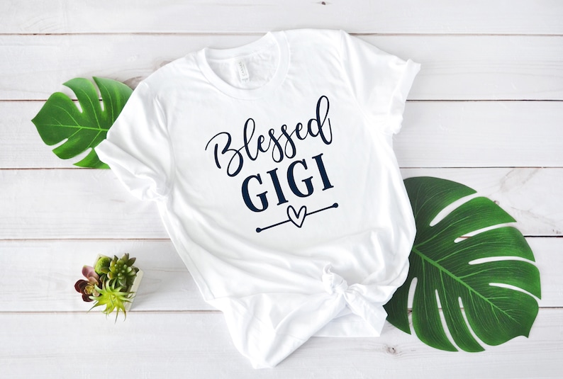 May include: White t-shirt with the text "Blessed Gigi" in navy blue lettering with a small heart graphic.