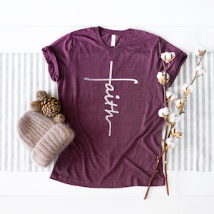 May include: A maroon t-shirt with a white cross and the word "faith" written vertically on the front.