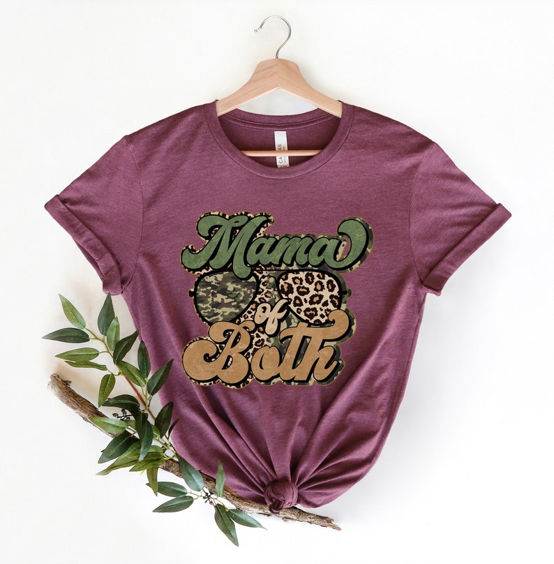 May include: A maroon t-shirt with the text "Mama of Both" in a retro font. The text is surrounded by a camouflage print and a leopard print.