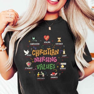 May include: Black t-shirt with the words "Christian Nursing Values" in colorful text. The shirt features illustrations of a stethoscope, heart, dove, and other symbols representing compassion, healing, peace, and other values.