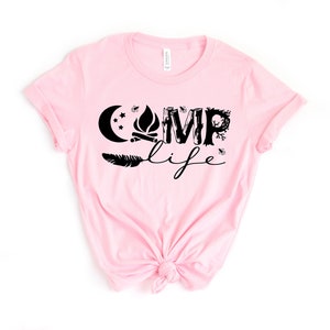 May include: Pink t-shirt with a black graphic design that says "Camp Life" with a moon, stars, campfire, feather, and trees.