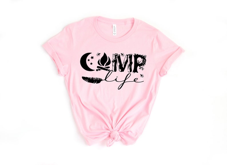 May include: Pink t-shirt with a black graphic design that says "Camp Life" with a moon, stars, campfire, feather, and trees.