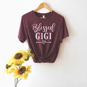 May include: Burgundy t-shirt with the text "Blessed Gigi" in pink lettering and a small pink heart.